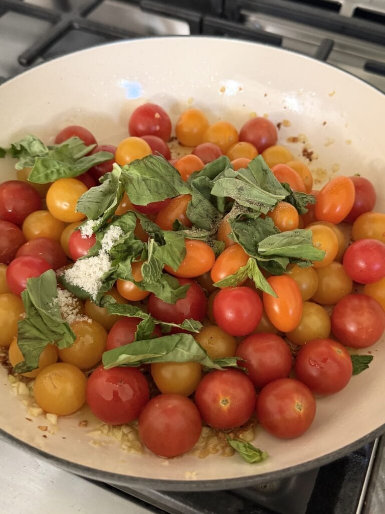 Tomatoes and fresh basil added to garlic in pan.