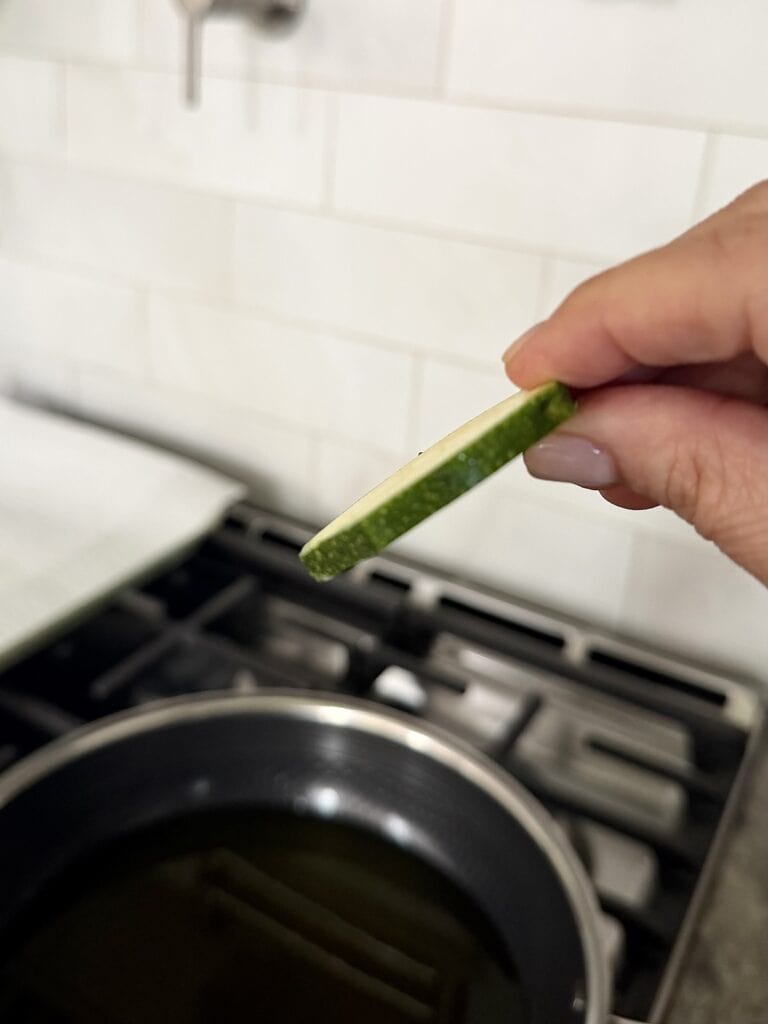 One zucchini slice held in hand to show correct thickness.