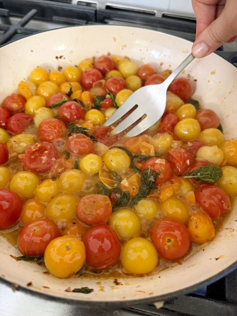 Lightly smashing burst cherry tomatoes with fork.