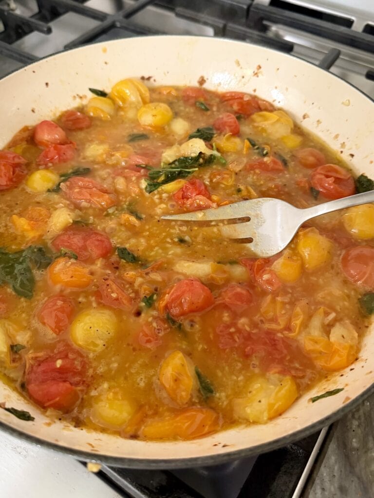 Lightly smashing blistered cherry tomatoes with fork as sauce simmers.