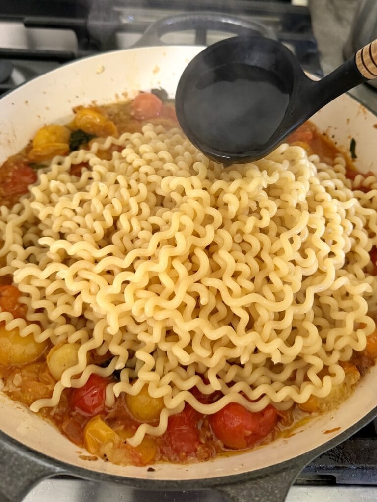 Adding pasta water to Burrata with Pasta and cherry tomatoes.