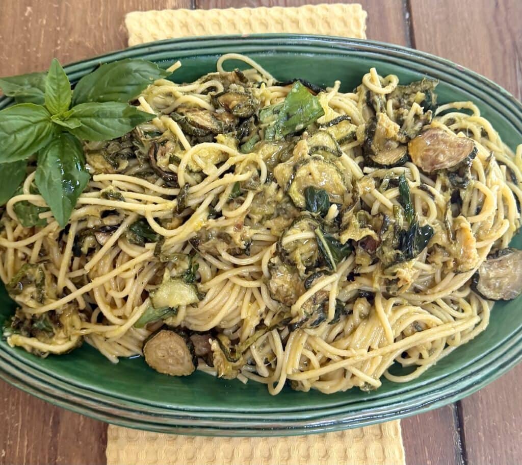 Nerano pasta in green serving platter over yellow towel with basil garnish.