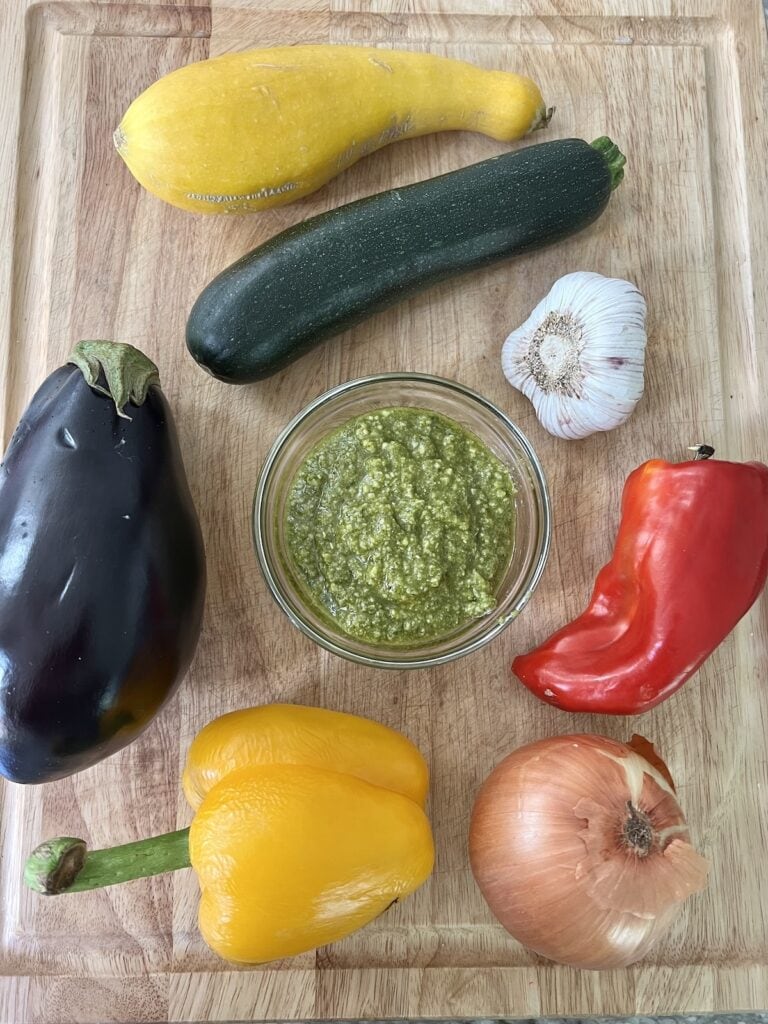 All ingredients for pesto roasted vegetables with zucchini on cutting board.