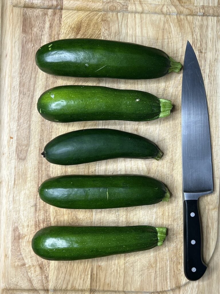 Five zucchni on a cutting board next to a chef's knife.