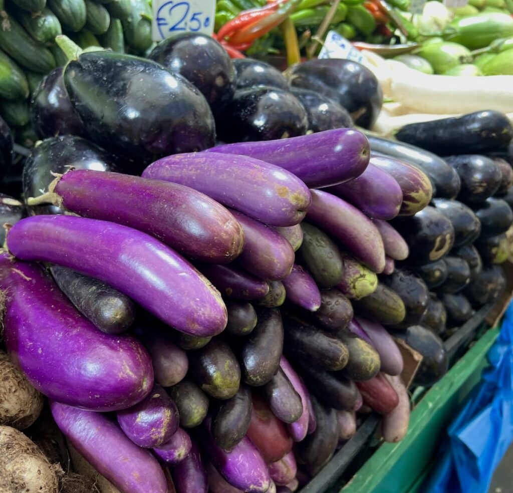 Piles of eggplant at outdoor market in Italy.