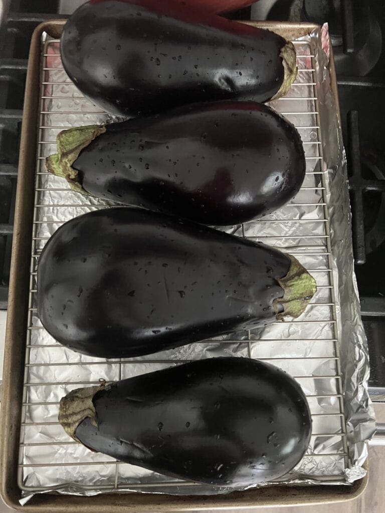 Four large globe eggplant on baking rack over foil lined sheetpan.