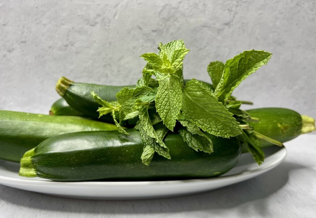 An assortment of garden zucchini with fresh mint in a white dish.