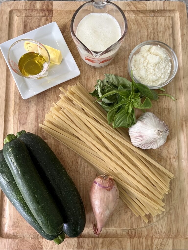All ingredients for creamy zucchini pasta on cutting board.