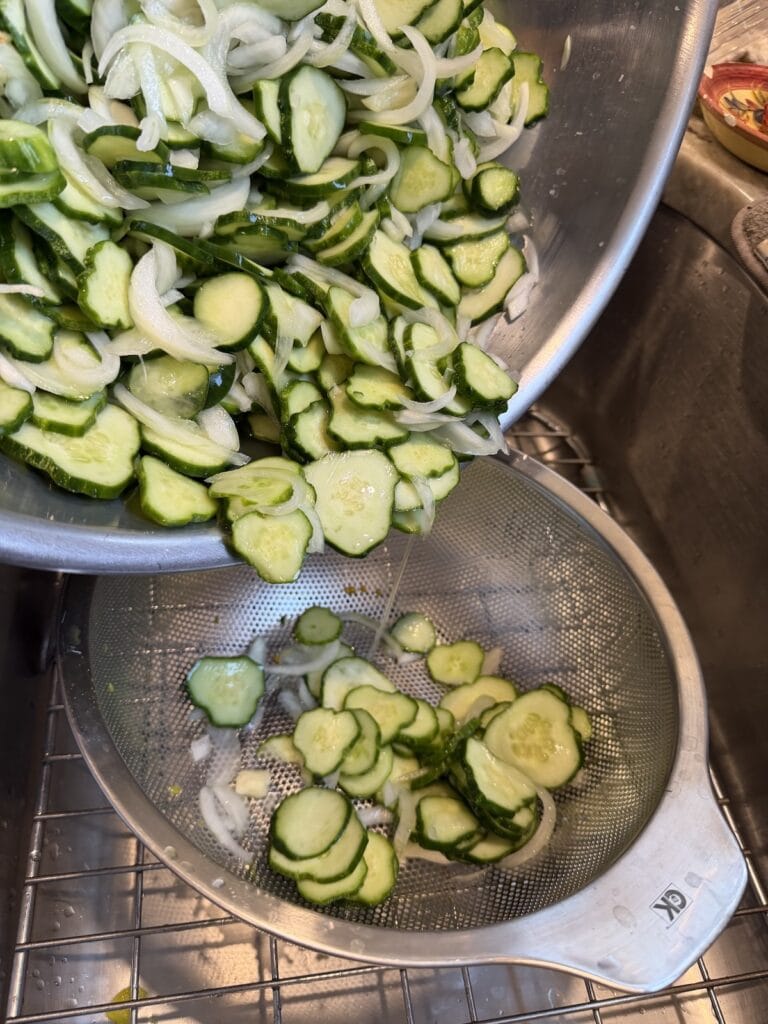 Puring the mixture for bread and butter pickles into a colander in sink to strain.