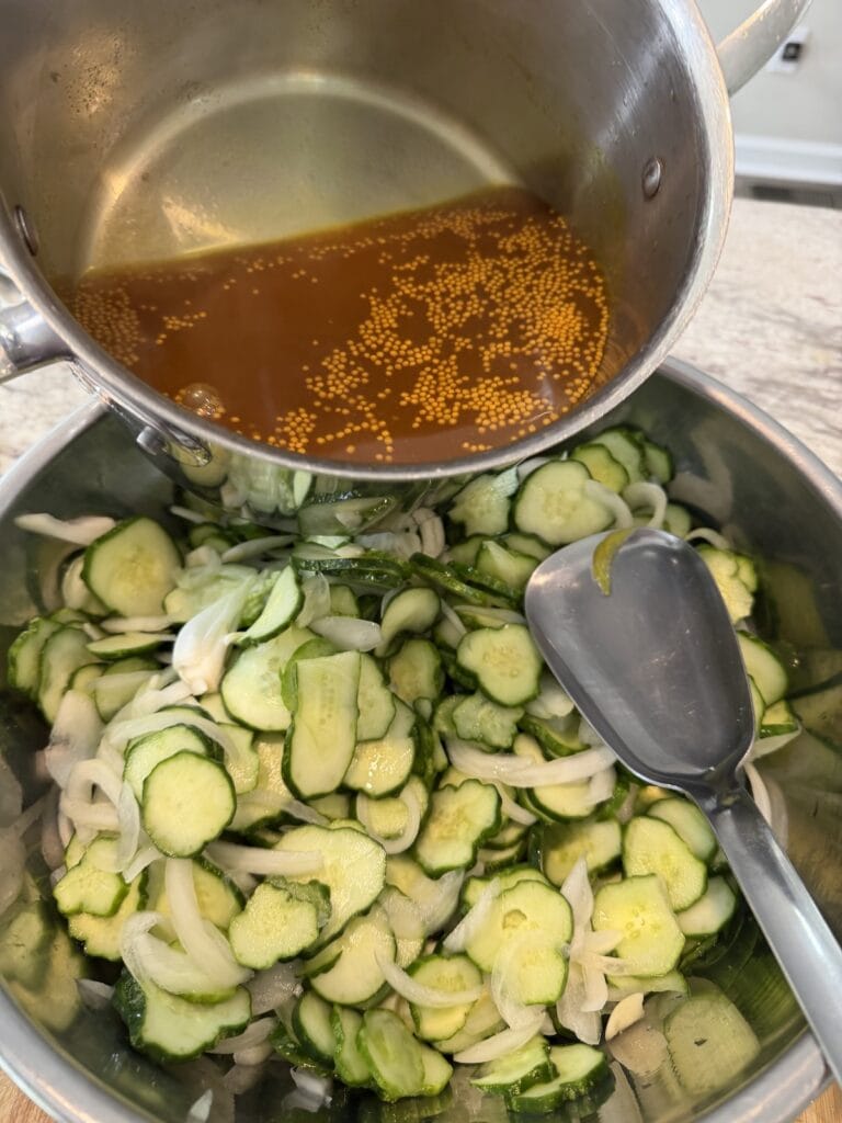 Pouring hot pickle brine over bowl of drained cucumber onion mixture.