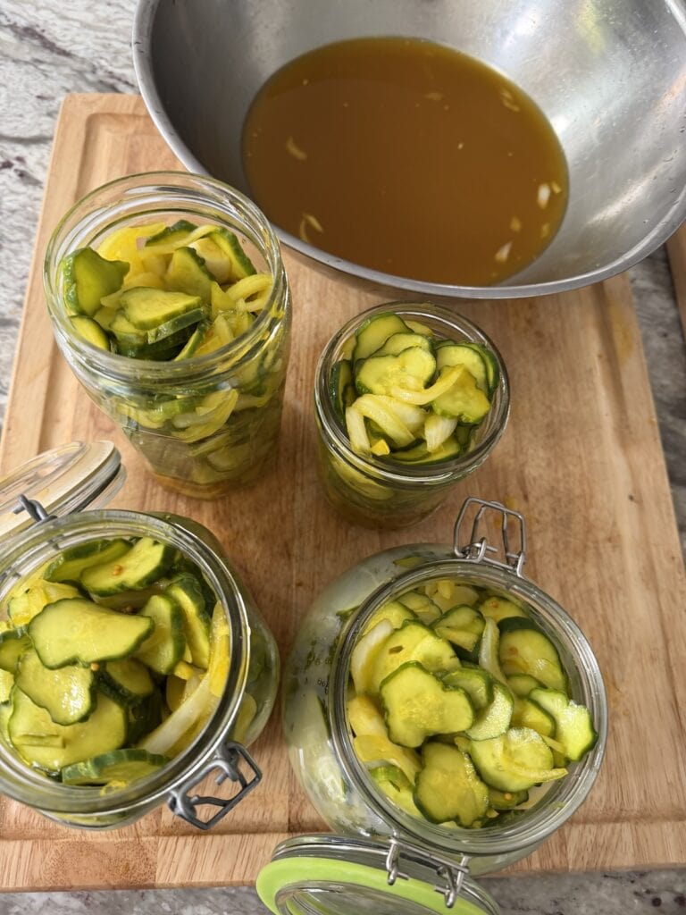 Overhead photo of four jars of refrigerator bread and butter pickle recipe with bowl of brine next to it.