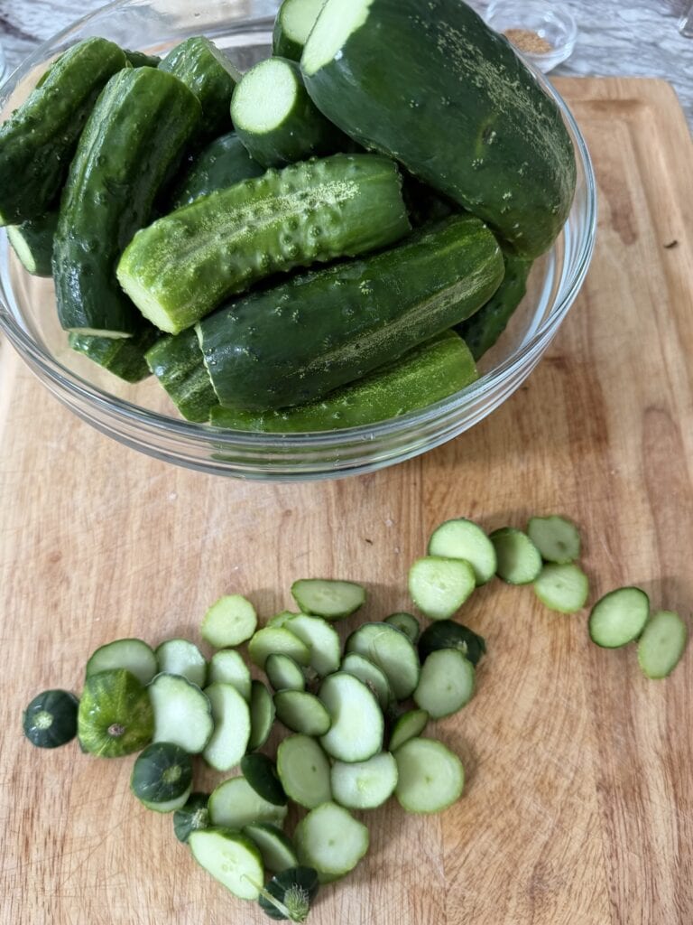 Ends of cucumbers on cutting board with bowl of raw cucumbers next to it.