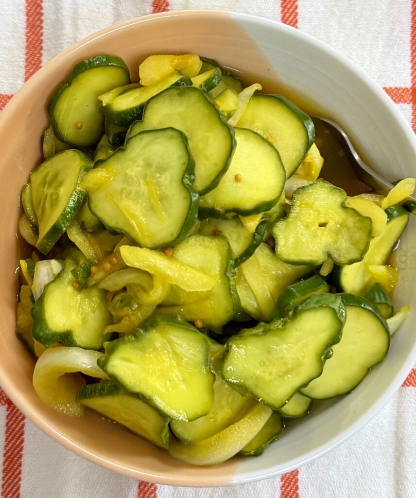 Homemade bread and butter pickles in bowl over decorative towel.