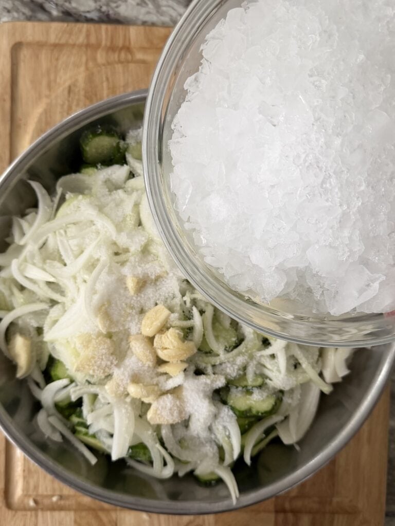 Crushed ice being added to bowl of sliced cucumbers.