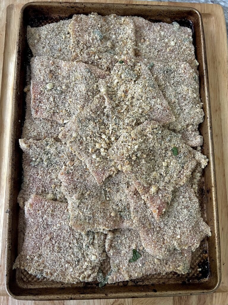 Breaded pork cutlets on baking sheet, ready to fry.