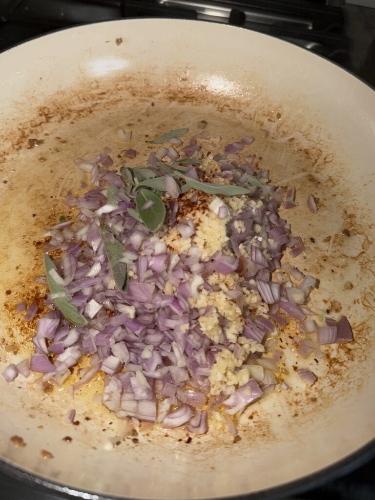 Sautéing aromatics (shallots, garlic, sage and crushed red pepper) in oil in pan.