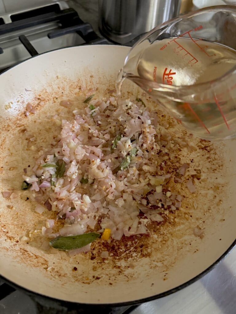 Adding white wine to pan to deglaze.