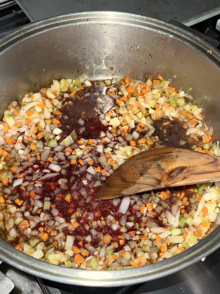 Red wine added to pot and wooden utensil being used to deglaze the pan.