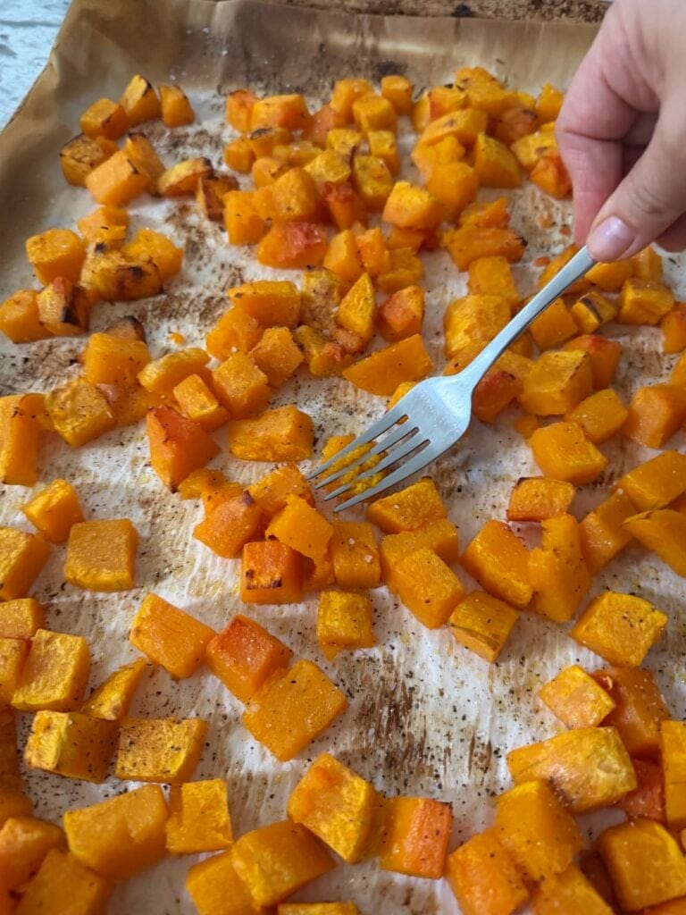 Mashing some of the roasted butternut with a fork on the baking sheet.