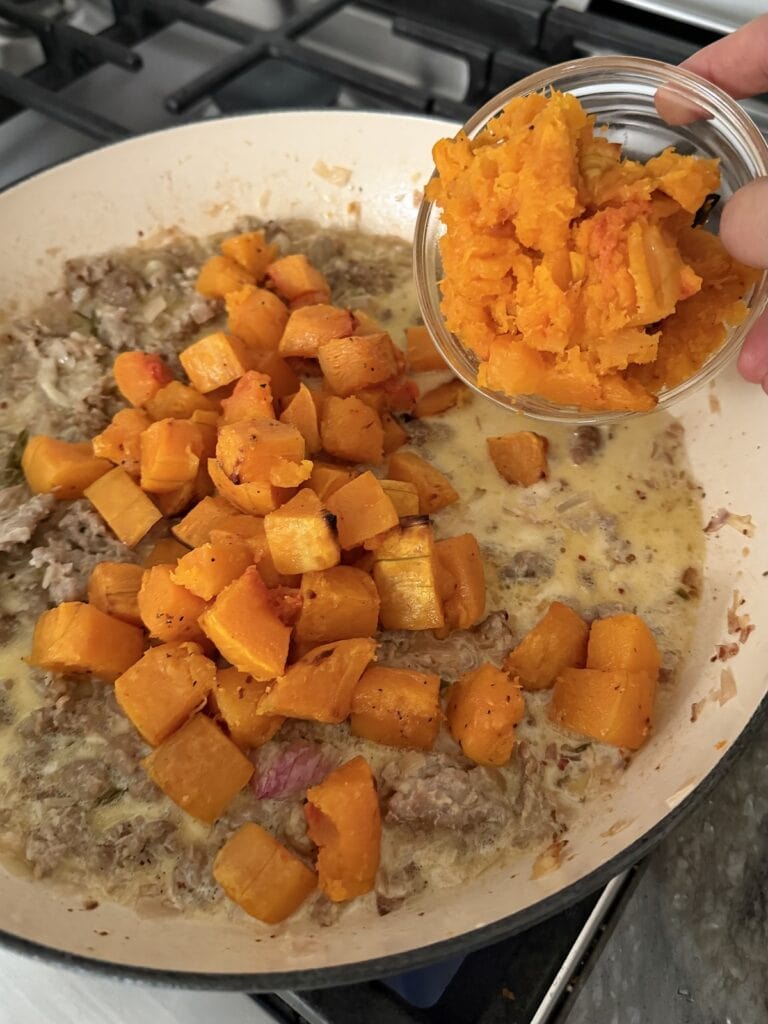 Adding the roasted butternut squash cubes and mash to pan to make sauce for butternut squash sausage pasta.