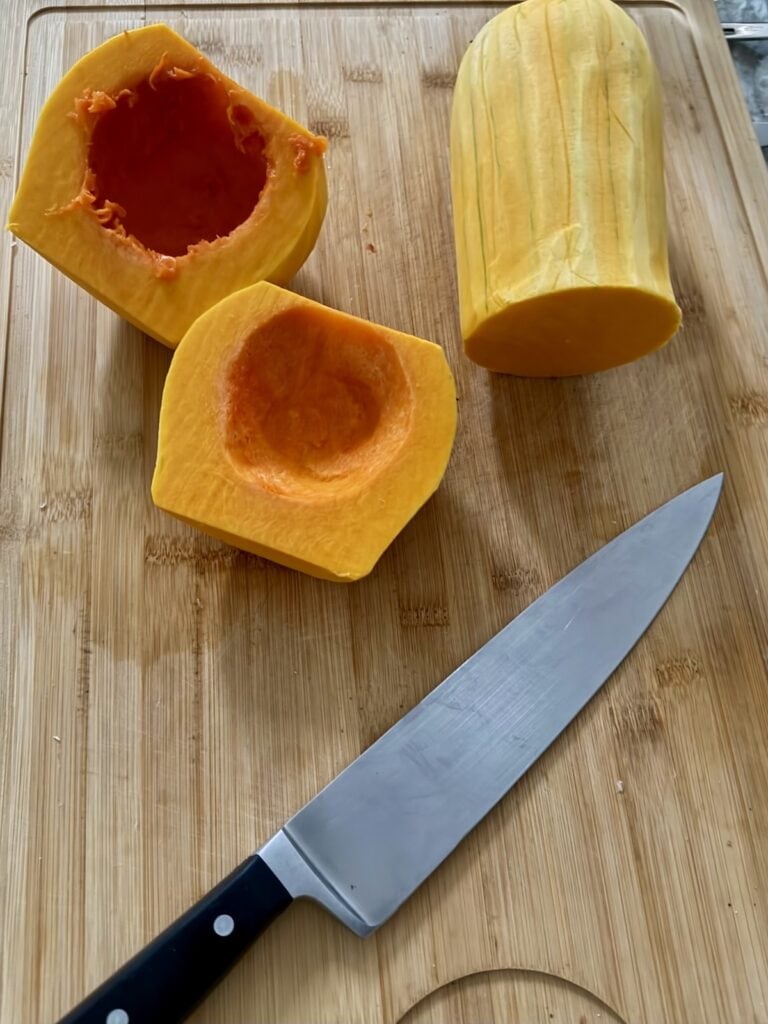 Knife + neck and 2 halves of globe of squash on cutting board.