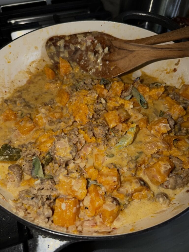 Stirring all components of creamy butternut squash sauce in pan.