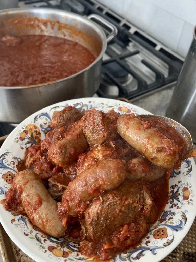 All the cooked braised meats removed from pot of gravy and transferred to a bowl, with remaining pot of sauce in background.
