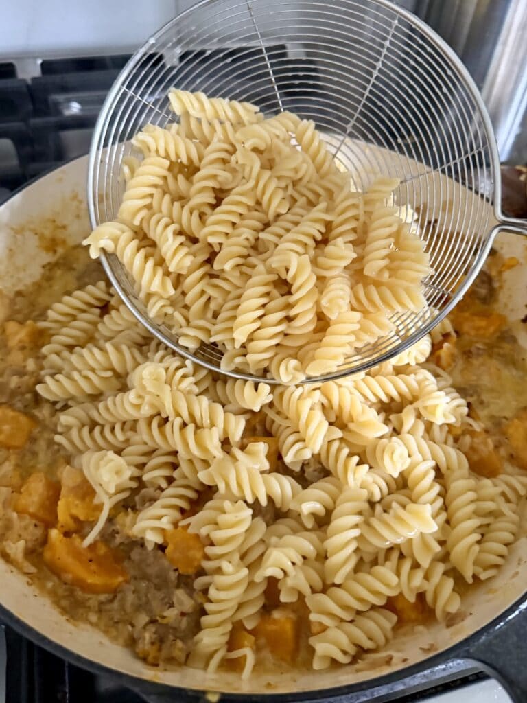 Adding cooked pasta to sauce in pan with spider.