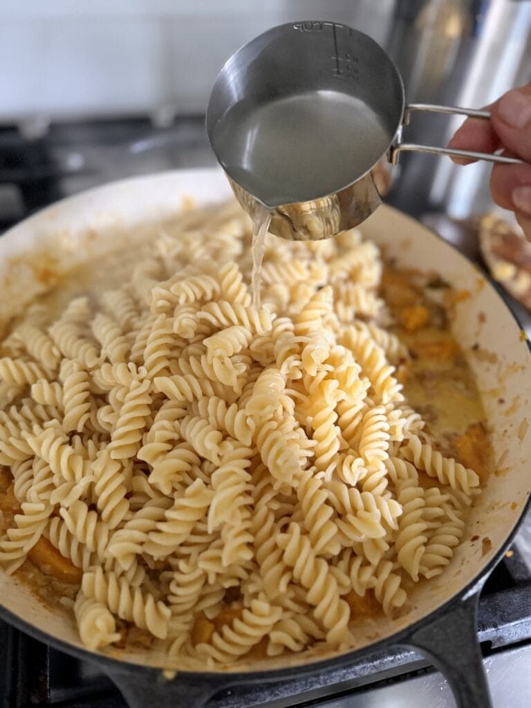 Pouring in some pasta water to moisten sauce.
