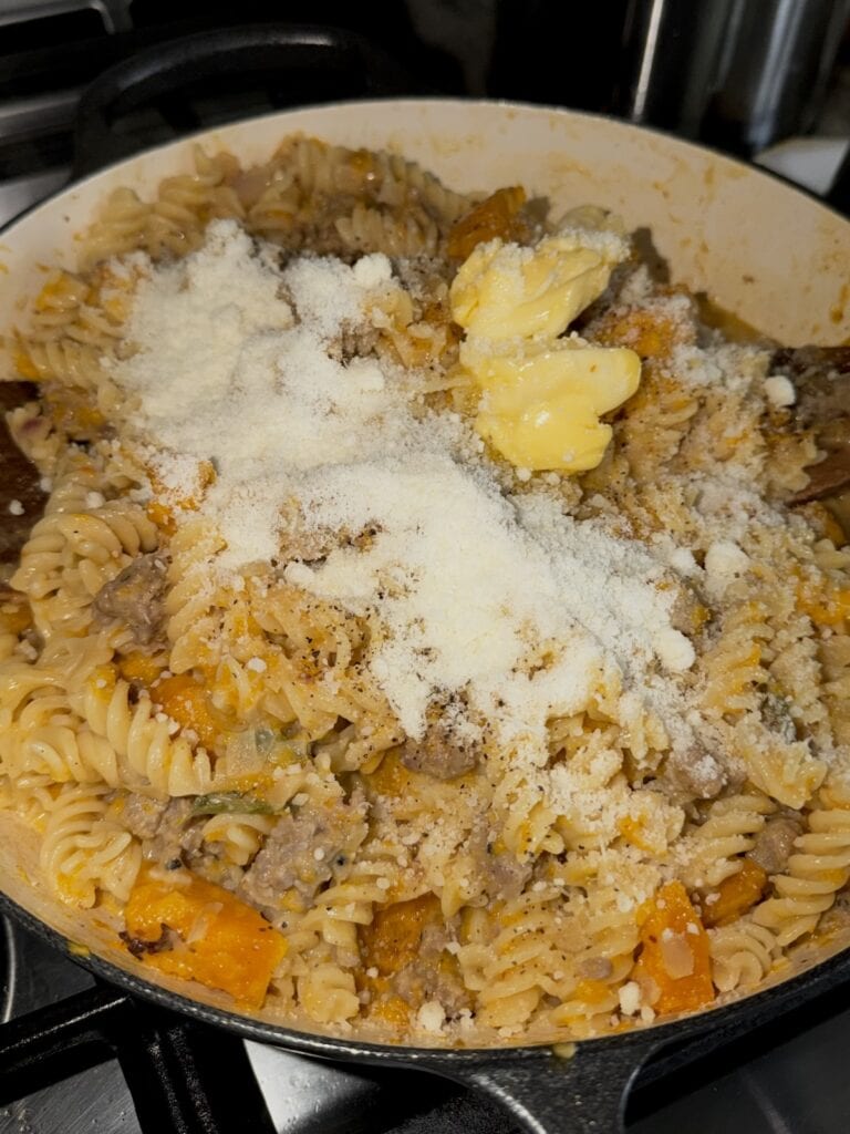 Butter and grated cheese added to butternut squash and sausage pasta in pan off the heat.
