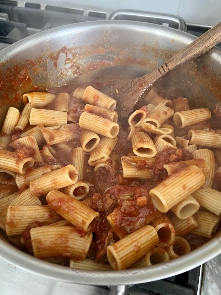 Mixing up the italian american red gravy in pot with wooden spoon.
