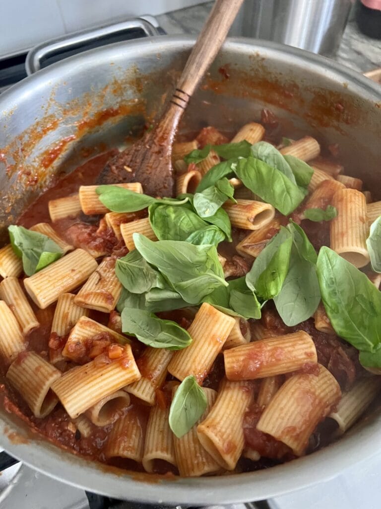 Fresh basil leaves added to cooked pasta in sauce.