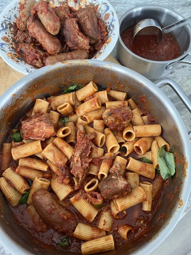 Overhead view of pot of sunday sauce with meat next to bowl of cooked meats and small pot of sauce only with ladle.
