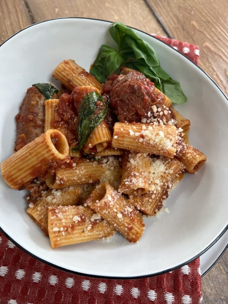 Authentic Italian Sunday Gravy in white pasta bowl with frsh basil garnish and grated cheese.
