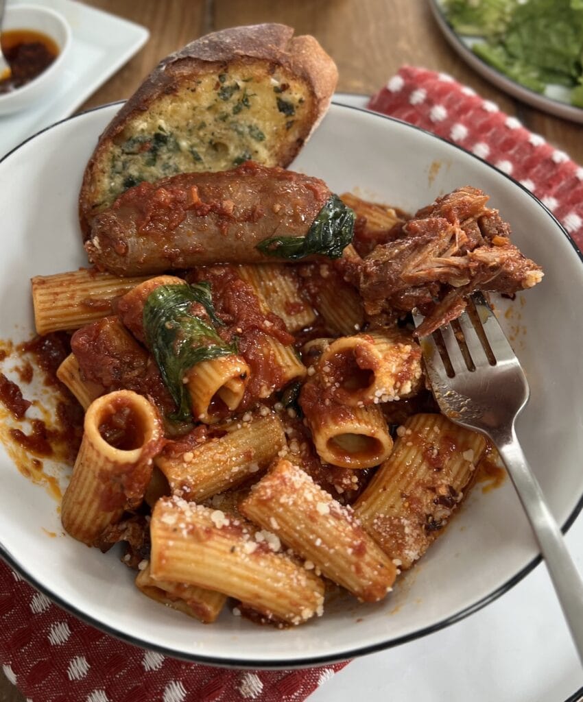 Pasta bowl filled with Authentic Italian Gravy and garlic bread with a hunk of braised meat on a fork.