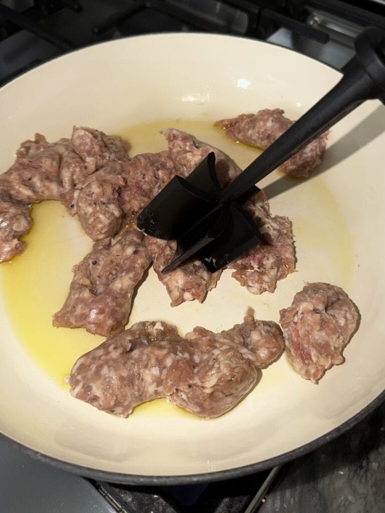 Breaking up bulk Italian pork sausage in pan with a meat chopper.