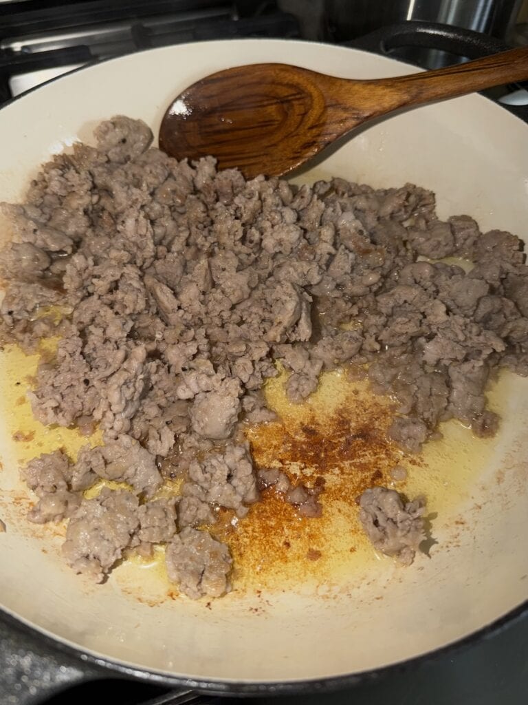 Browned sausage in pan with wooden spoon for butternut squash and sausage pasta.