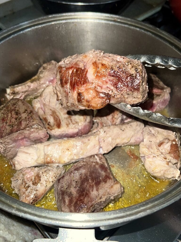 Turning a piece of meat over in pot with tongs.