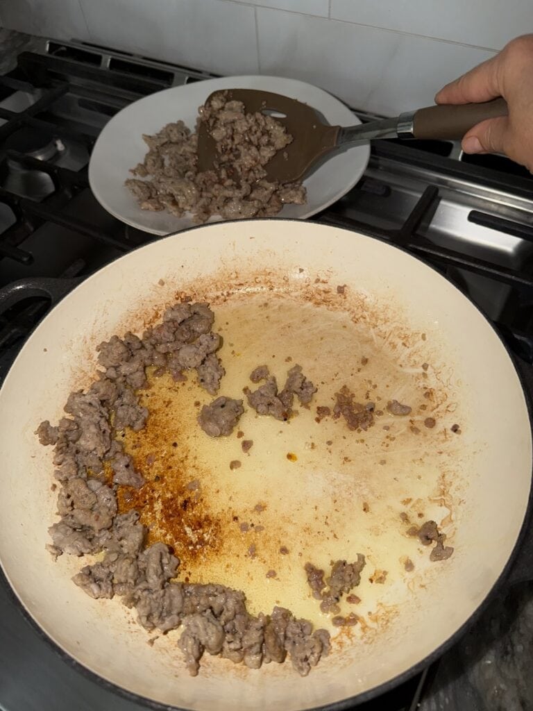 Transferring cooked sausage from pan to dish with wooden spoon.