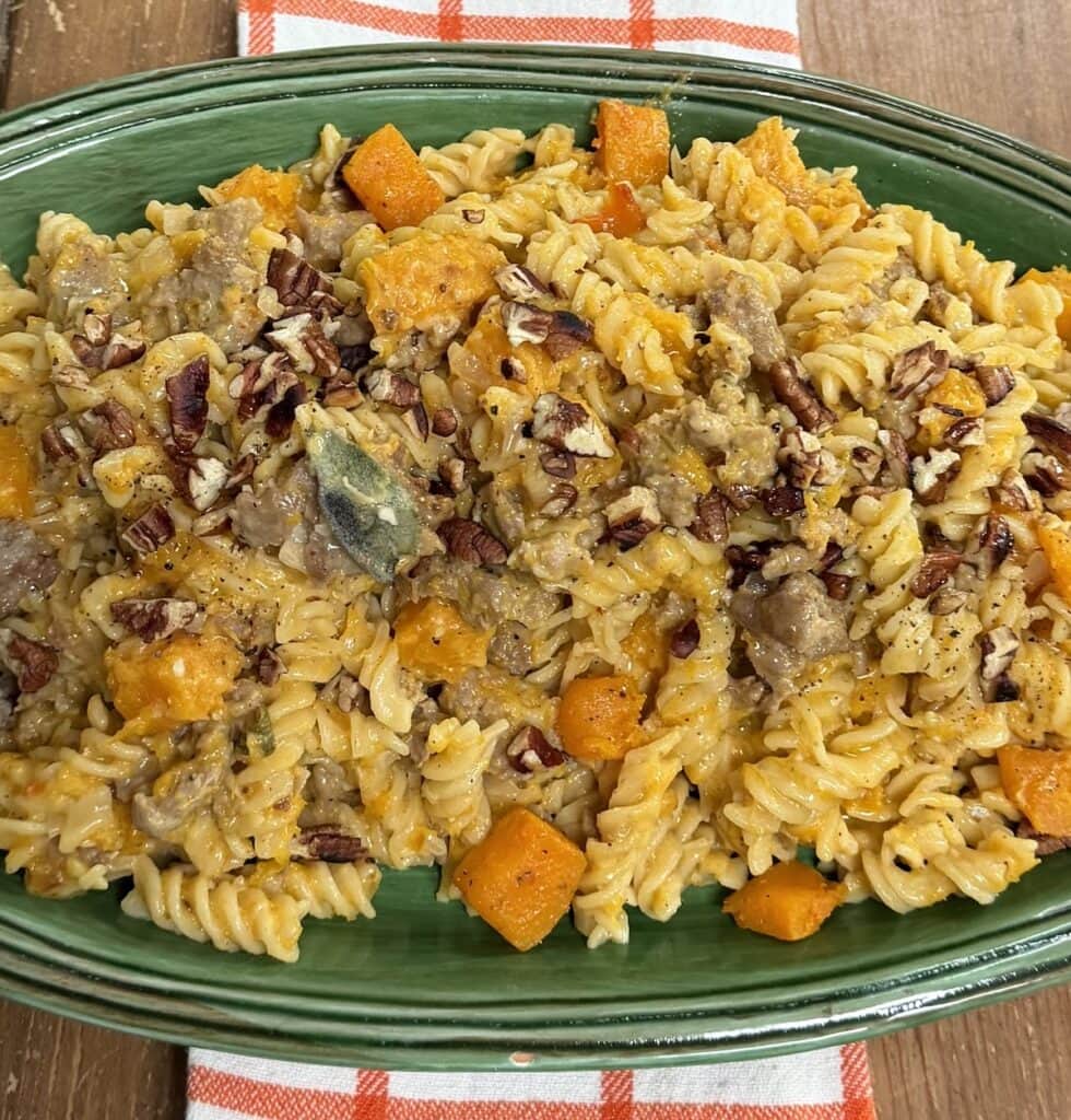 Creamy Butternut Squash and Sausage Pasta with sage and toasted pecans on green serving platter over decorative towel.