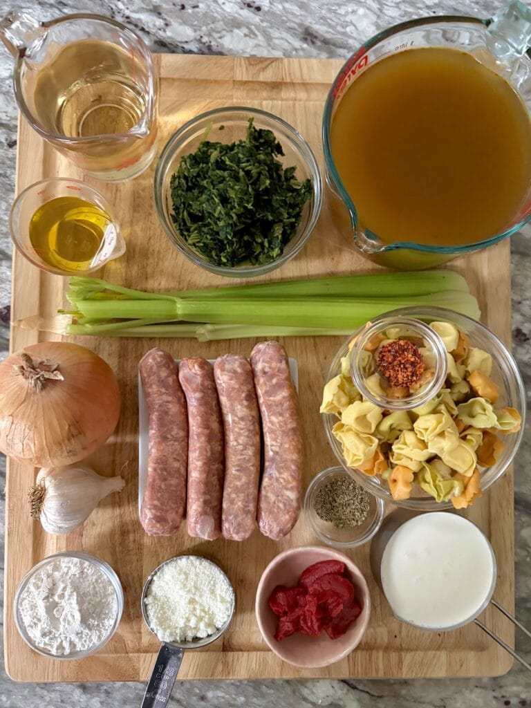 All ingredients for creamy tortellini soup with sausage and spinach on cutting board.