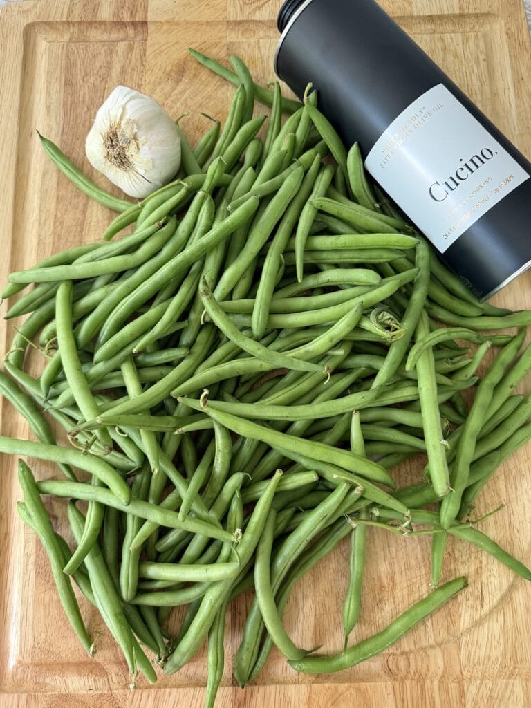 Garlic bulb, raw green beans and olive oil on cutting board.