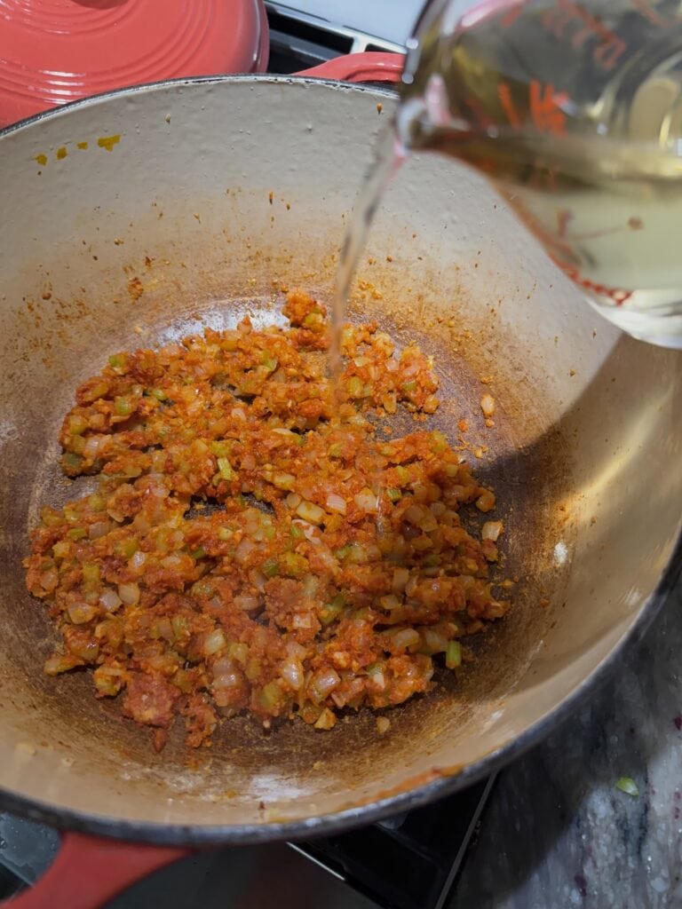 Pouring wine into pot to deglaze.