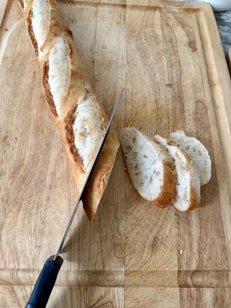 Slicing baguette with knife on cutting board.