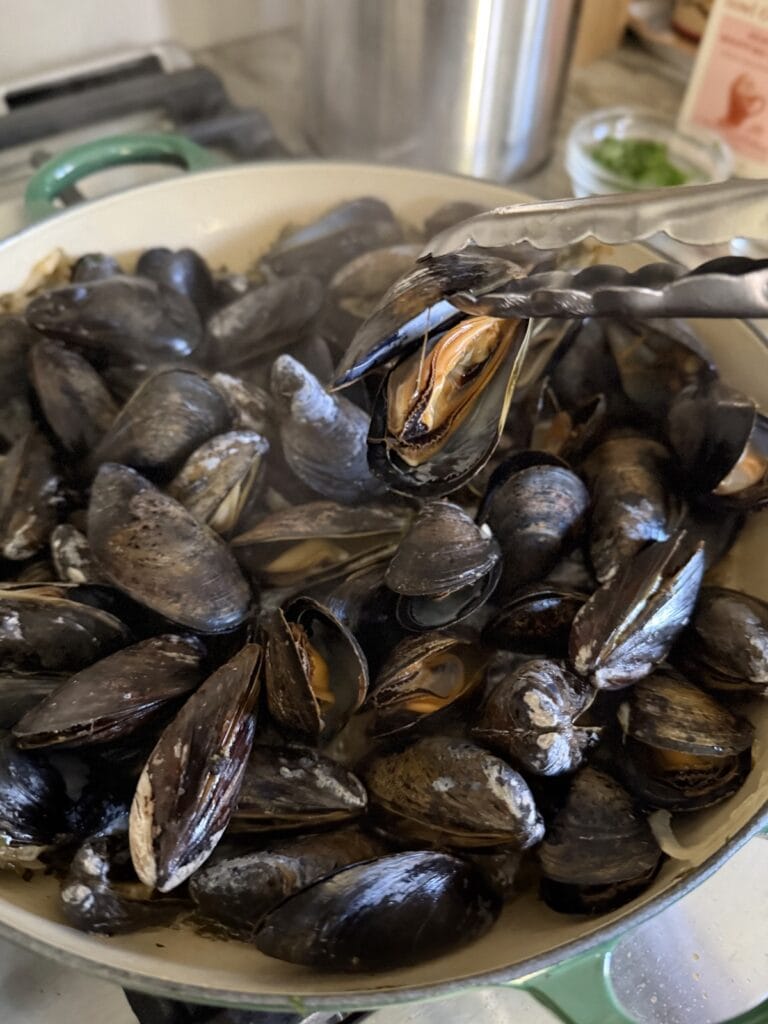 Transferring a cooked mussels out of pan with tongs.