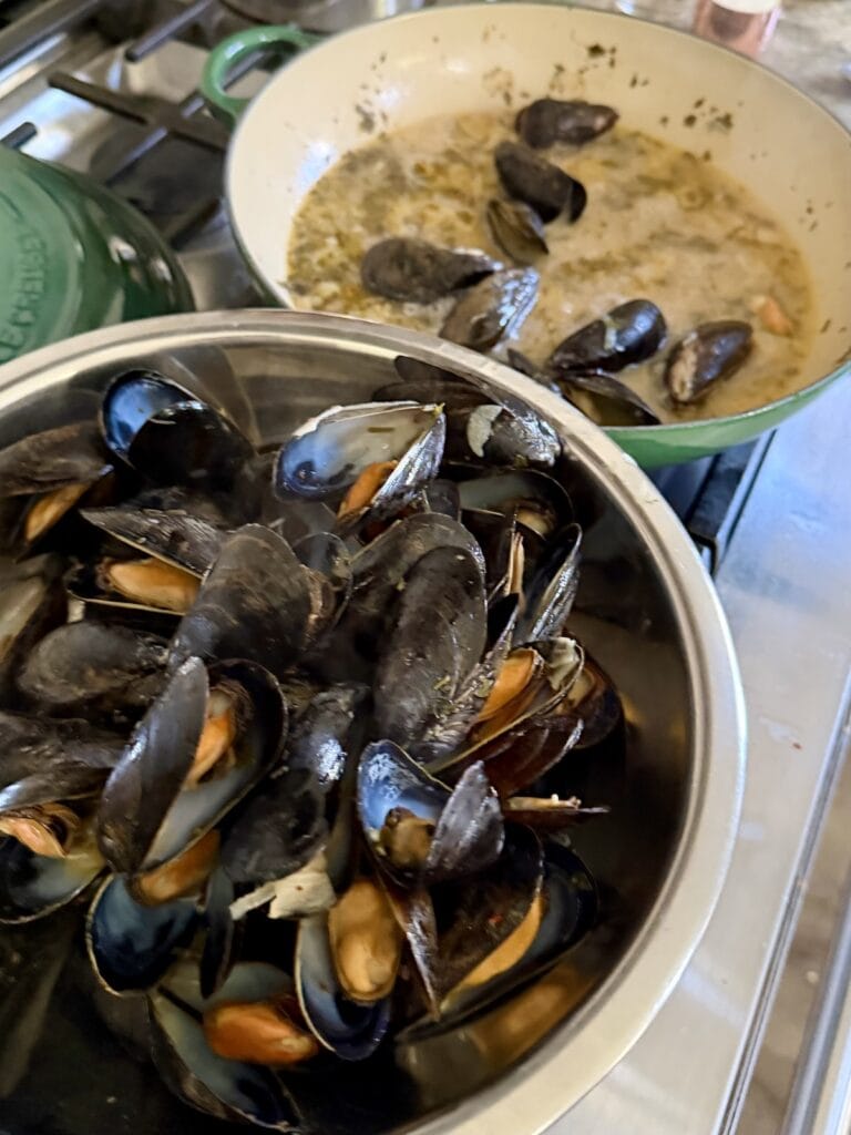 White zuppa di mussels in bowl with pan wih a few left cooking in the background.