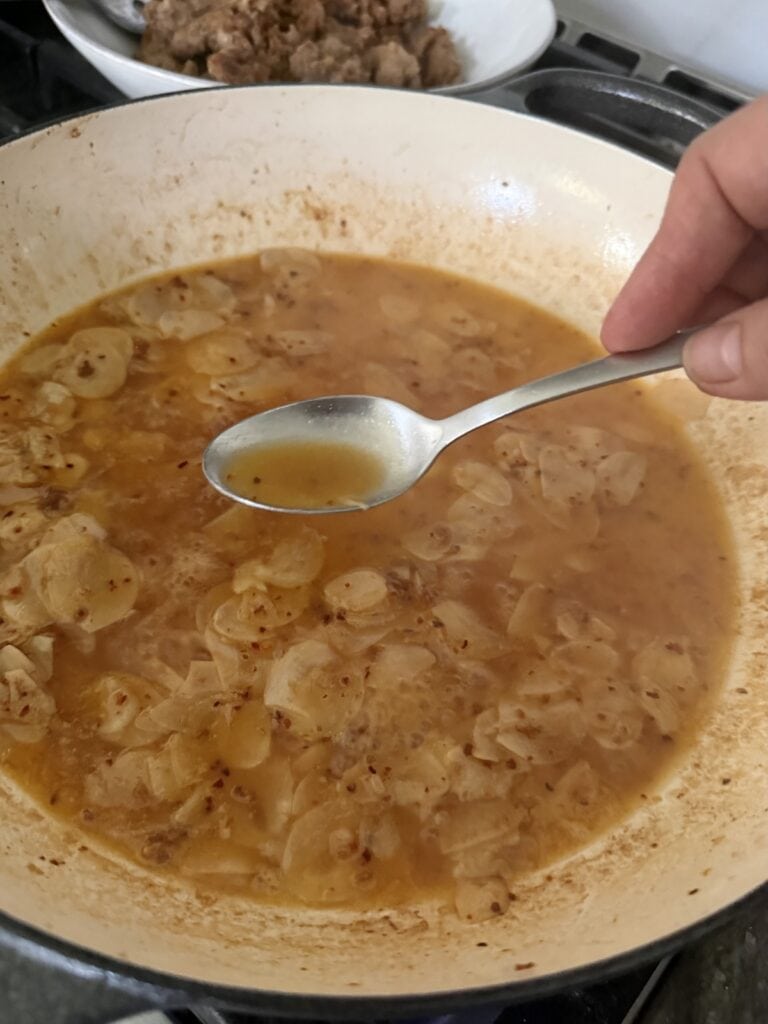 Testing the reduced wine in pan with the help of a spoon to see if the alcohol taste has cooked off.