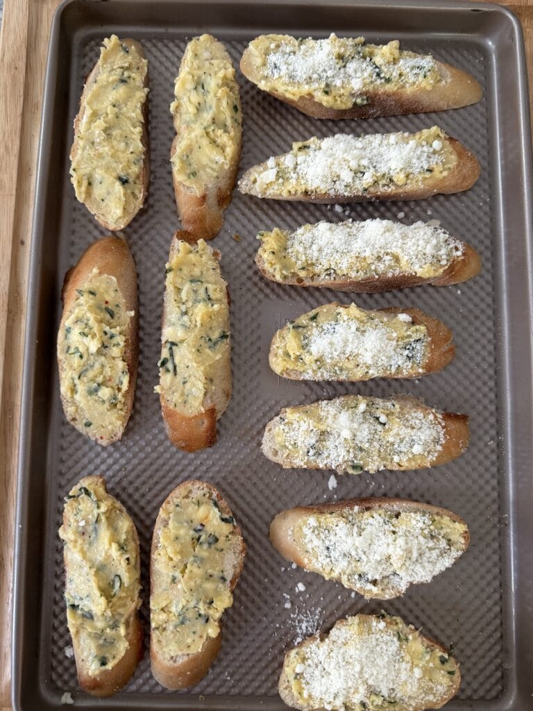 Buttered baguette slices on sheet pan ready to go into the oven