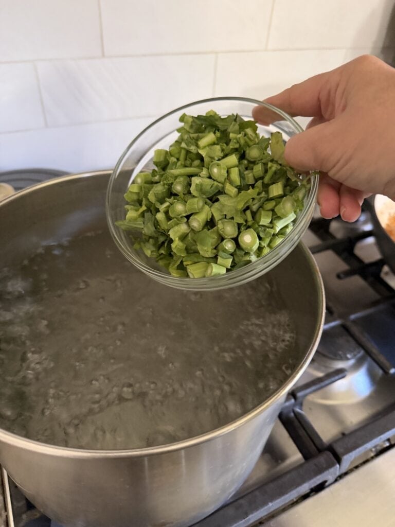 Adding chopped broccoli rabe stems to boiling water in pot.