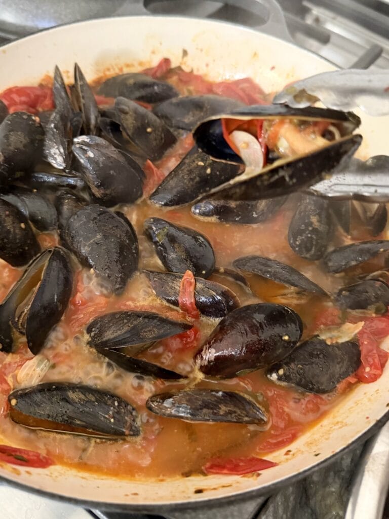Removing cooked mussel from pan with tongs.
